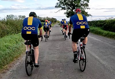 A group of cyclists riding down a straight road, two abreast